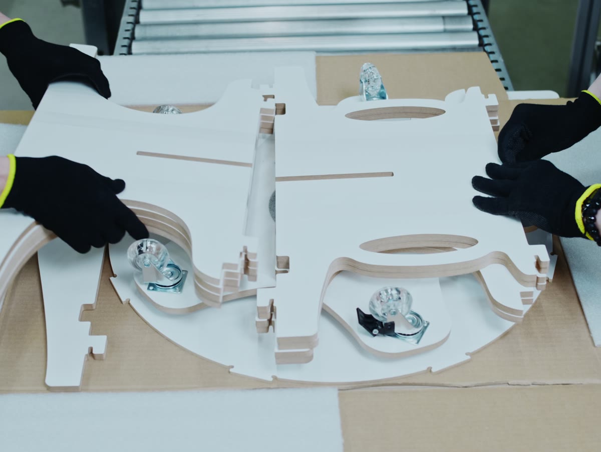 Two people in Piar gloves laying flat-packed MDF display parts into a shipping box.